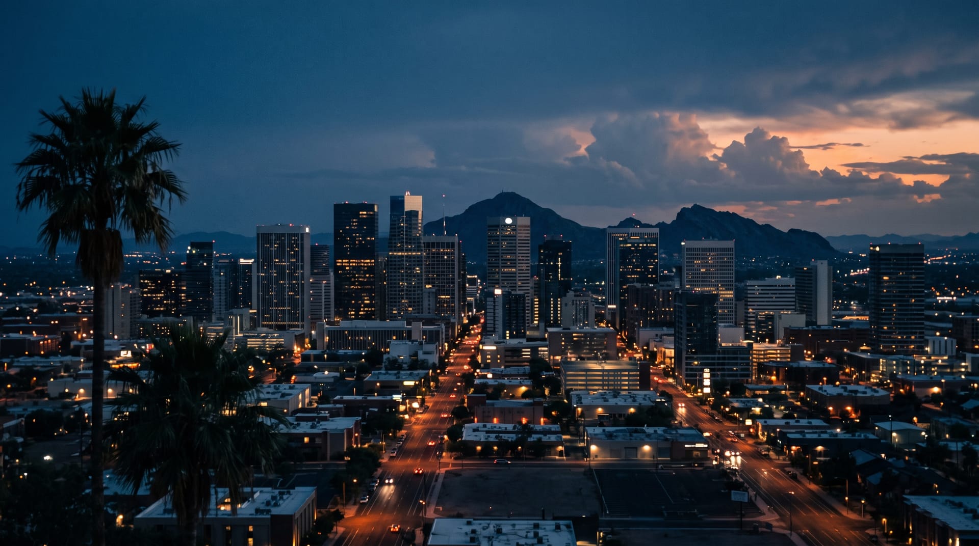 The downtown Phoenix skyline at blue hour with Camelback Mountain behind it and monsoon clouds catching the last light.